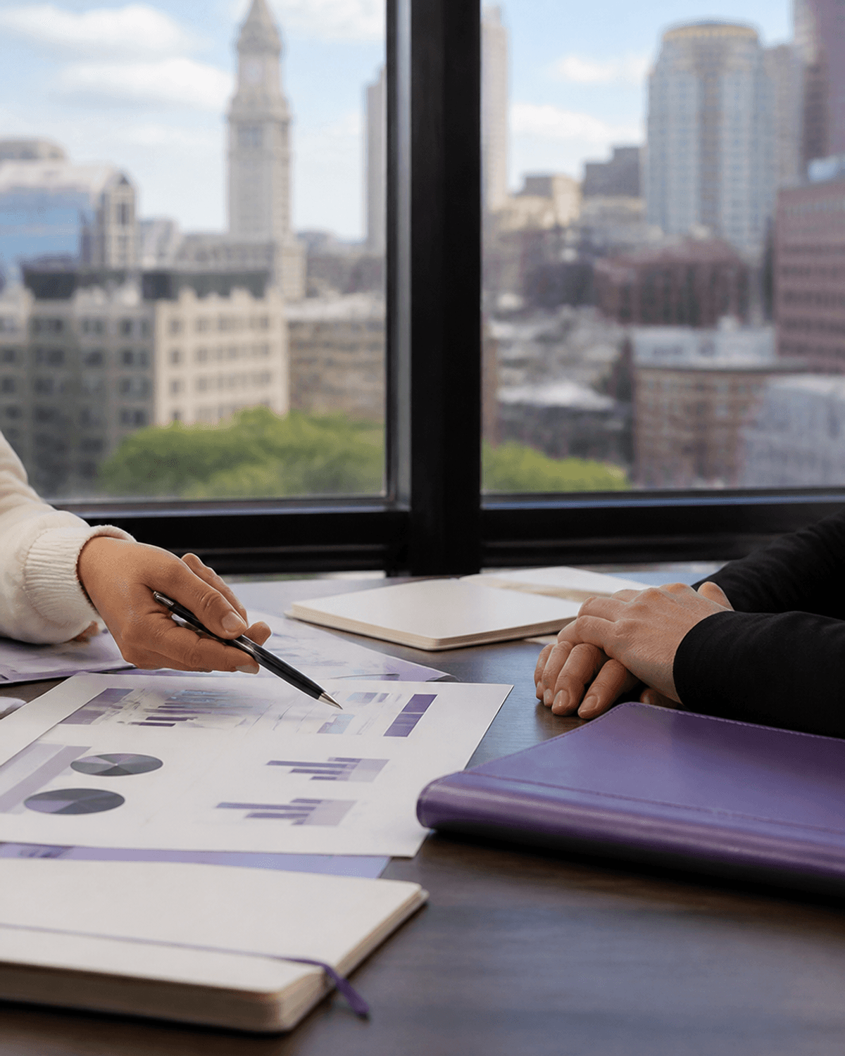 Hands reviewing abstract business growth charts with a purple portfolio in a Boston office